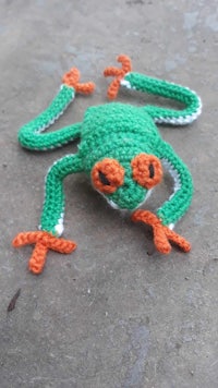 a crocheted frog laying on the ground